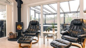 A modern living room with leather recliners, a wood-burning stove, a glass door leading outside, and a view of the outdoors. - Holiday Home in LÃ¦sÃ¸ (Læsø)