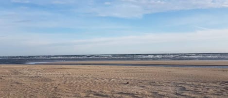 Uma praia com extensa faixa de areia e mar calmo sob um céu claro.