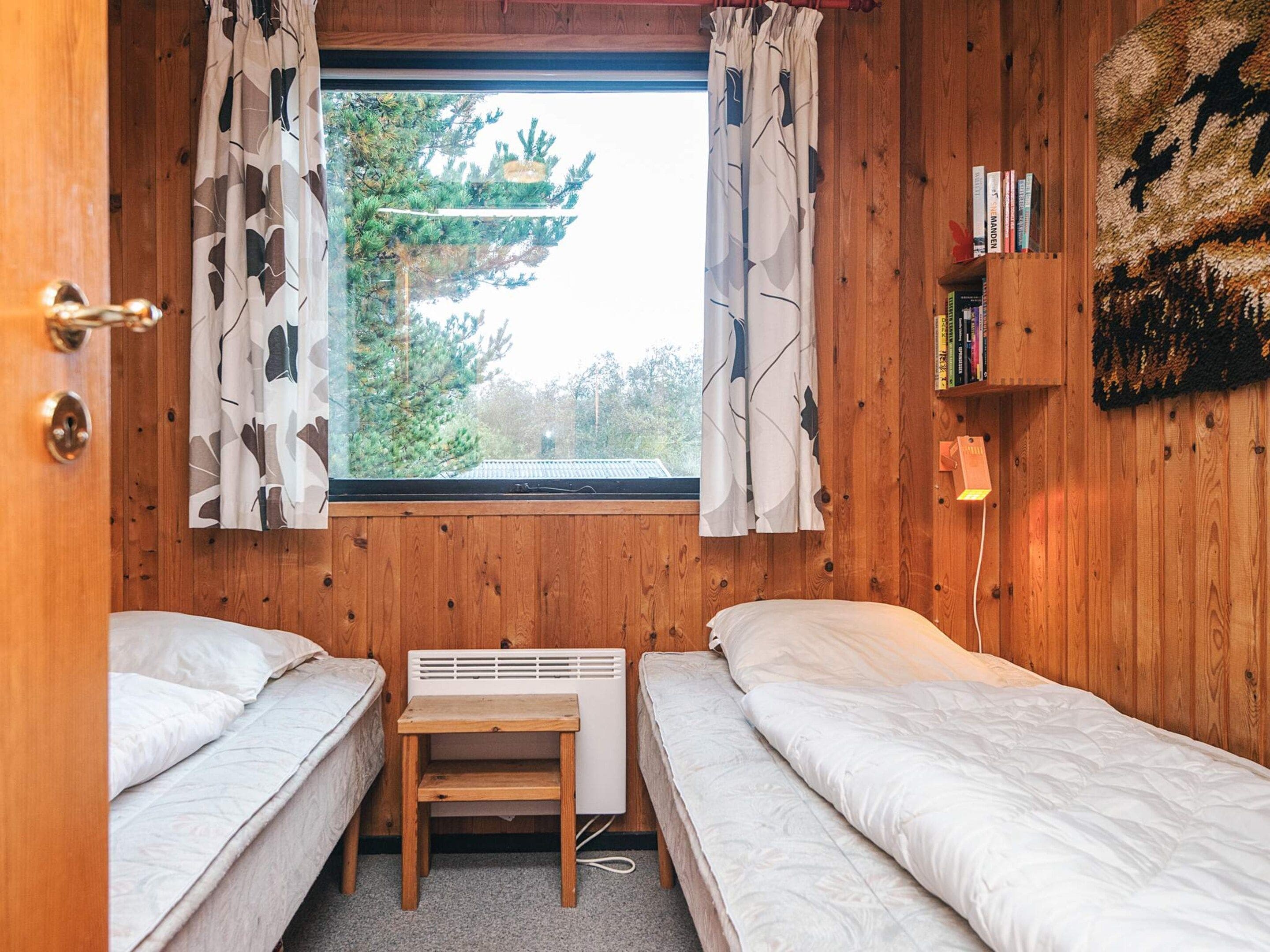 Une chambre avec deux lits, une petite table, un radiateur et une fenêtre avec des rideaux.