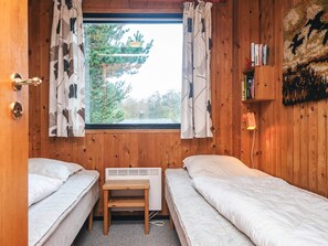 A room with two beds, a small table, a heater, and a window with curtains.