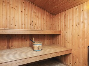 En træsauna med træbænk og en spand med træske.
