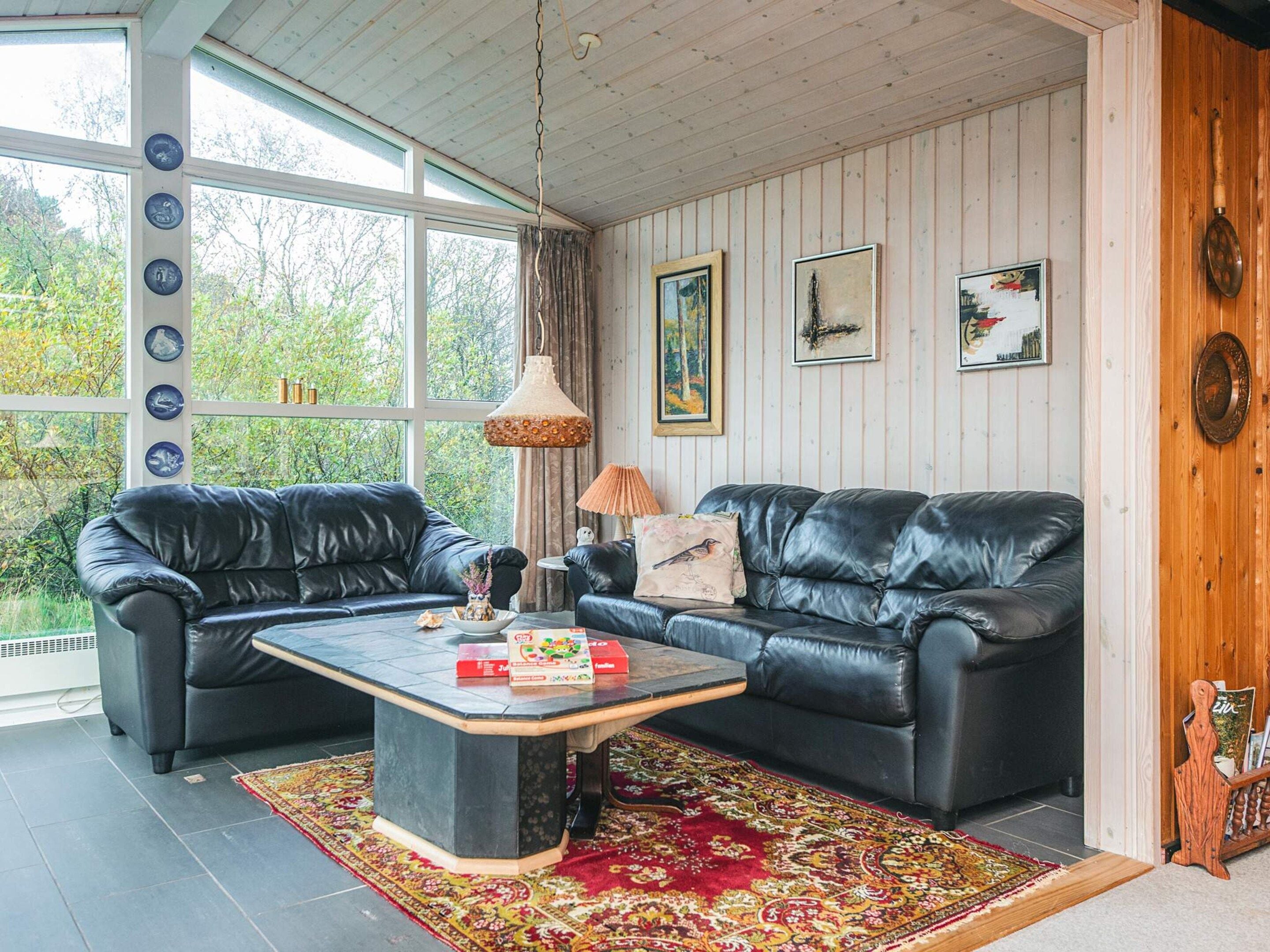 A living room with two black leather sofas, a coffee table, and a patterned rug. There are framed artworks on the wall and a wooden cabinet with decorative items.