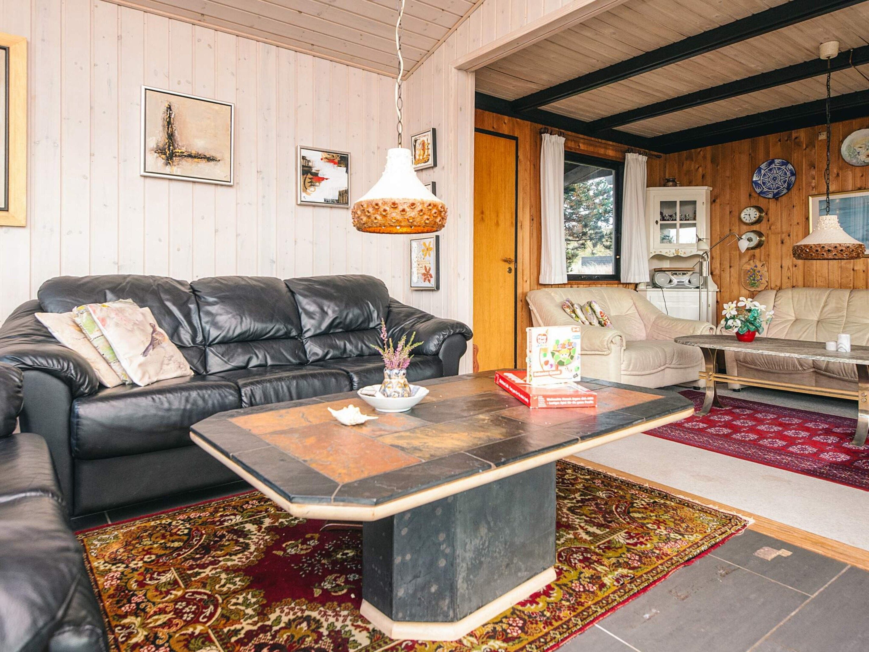 A living room with a black leather sofa, a coffee table, and a patterned rug.