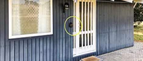 Un petit bâtiment d’un seul étage, à l’extérieur sombre, avec une fenêtre à cadre blanc, une porte ornée de barreaux verticaux et un petit porche.