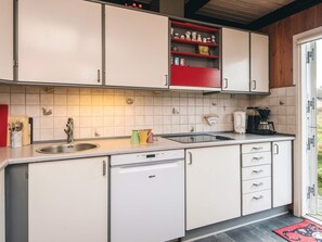 Una cocina compacta con armarios blancos, lavavajillas, cafetera y estante rojo con utensilios de cocina.