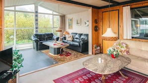 A spacious living room with a black leather sofa, a round coffee table, and a beige sofa. There are large windows providing natural light and a view of greenery outside. - 4 Person Holiday Home in Fano (Fano)