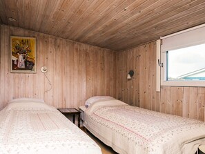 A room with two beds, wooden walls, a window, and a painting on the wall.