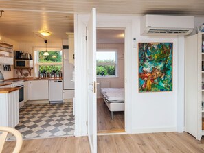 A compact kitchen with white cabinets, a microwave, and a window with a view of greenery. A door leads to a bedroom with a bed and a window. - 6 Person Holiday Home in Fano (Fano)