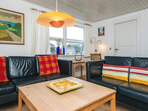 A living room with two black leather sofas, a wooden coffee table, a large painting on the wall, and a window with curtains. - 6 Person Holiday Home in Fano (Fano)