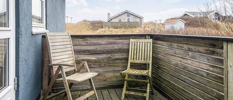 A wooden deck with two chairs and a table, overlooking a grassy area with a house in the background.