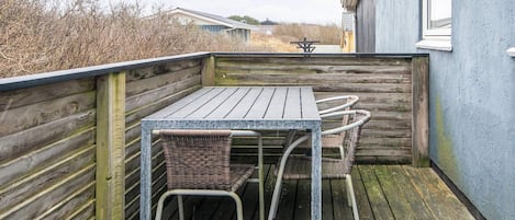 A wooden deck with a table and two chairs, a metal railing, and a building in the background.