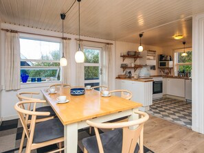 A dining area with a wooden table and chairs, a kitchen with white cabinets, and a checkered floor. - 6 Person Holiday Home in Fano (Fano)