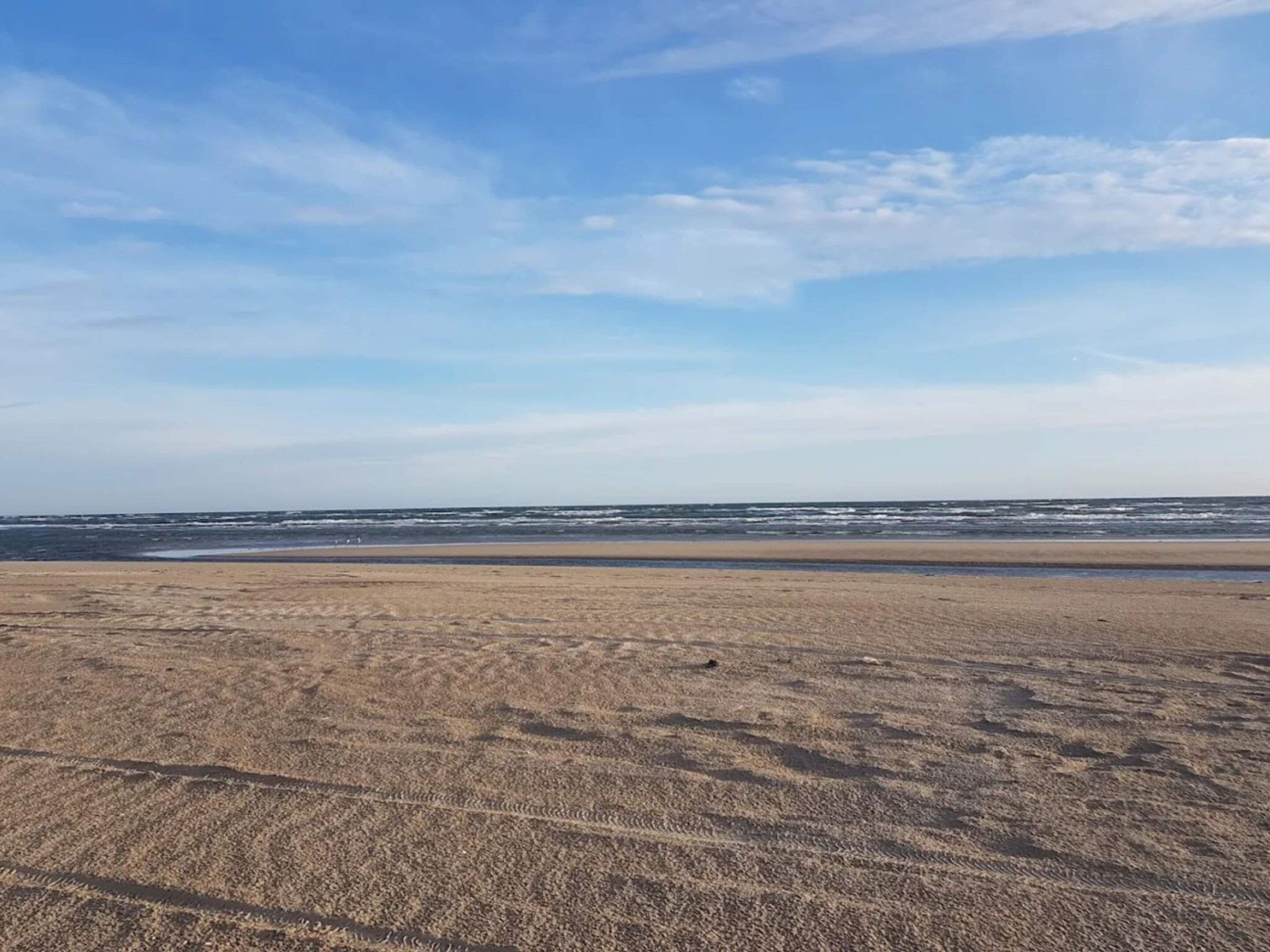 Een strand met een breed zandgebied en een rustige zee onder een heldere lucht.