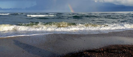 A beach with waves, pebbles, and a rainbow.