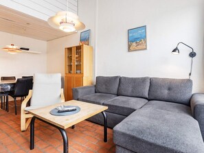 Ein modernes Wohnzimmer mit einem grauen Sofa, einem Holztisch und einem Essbereich mit einem weißen Stuhl und einem Holzschrank.