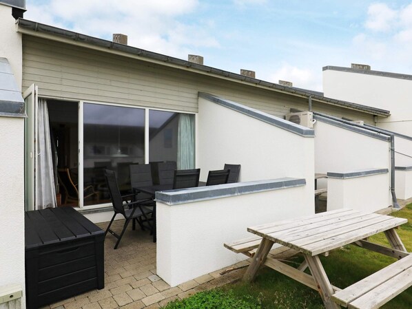 A patio with a table and chairs, a black storage unit, and a sliding glass door leading to an interior space.