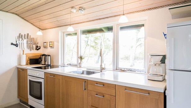 A modern kitchen with wooden cabinets, a stainless steel sink, and a built-in oven. - Secluded Pine Tree Cottage-by Traum (Blavand)