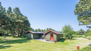 A small, single-story cabin with a red door and a metal roof, surrounded by a grassy area and trees. - Secluded Pine Tree Cottage-by Traum (Blavand)