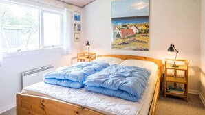 A bedroom with a wooden bed, two bedside tables, a window, and a painting on the wall. - Secluded Pine Tree Cottage-by Traum (Blavand)