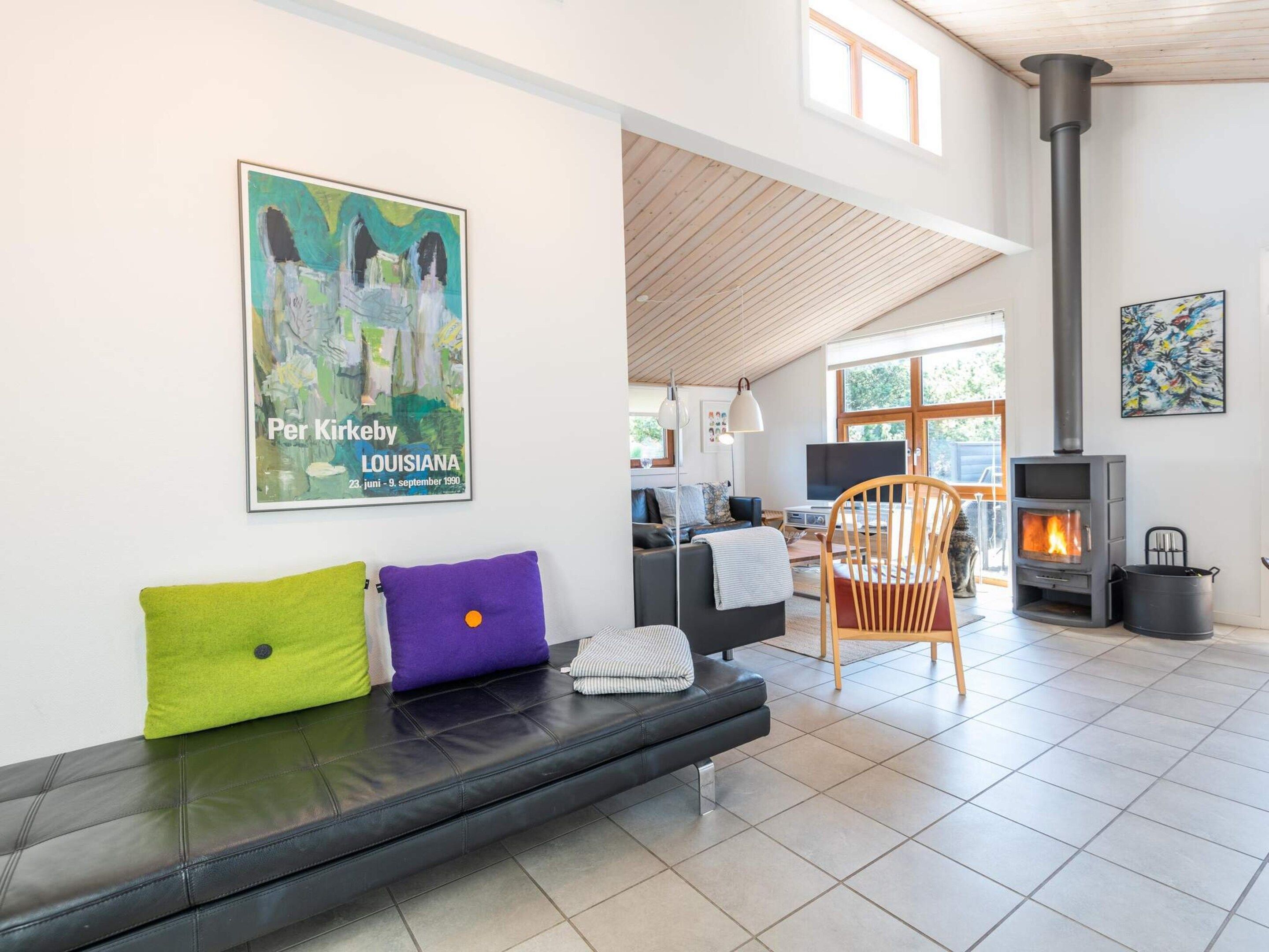 A modern living room with a black leather sofa, a wooden chair, a fireplace, and a poster on the wall.