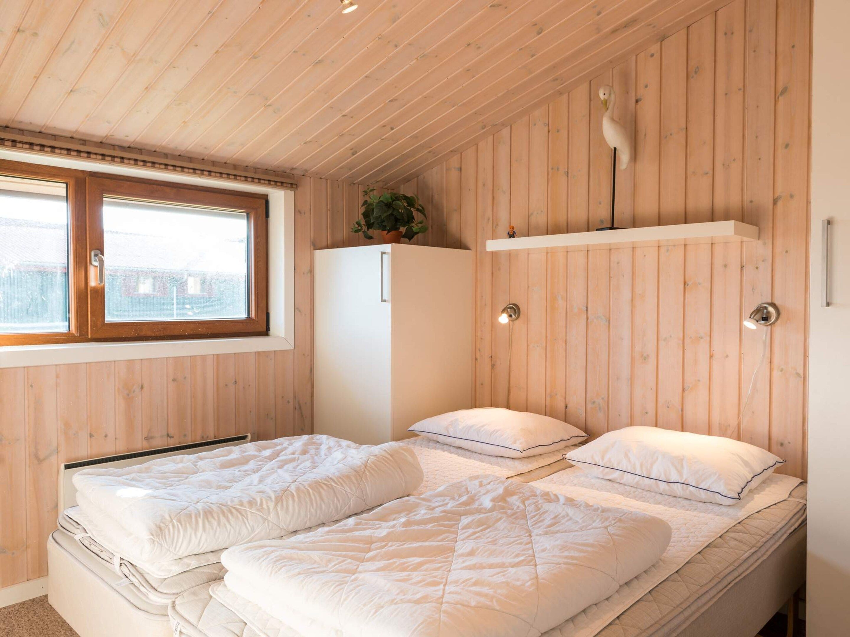 Een slaapkamer met twee bedden, een raam, een koelkast en een plank met een plant.