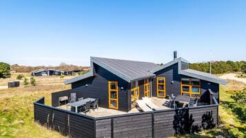 A modern two-story house with a flat roof, large windows, and a patio area with outdoor furniture.