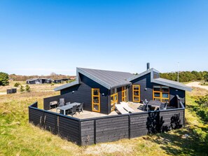 Uma casa moderna de dois andares com telhado plano, janelas amplas e um espaço de varanda com mobiliário de exterior.