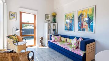A living room with a blue sofa, wicker furniture, and artwork on the walls.