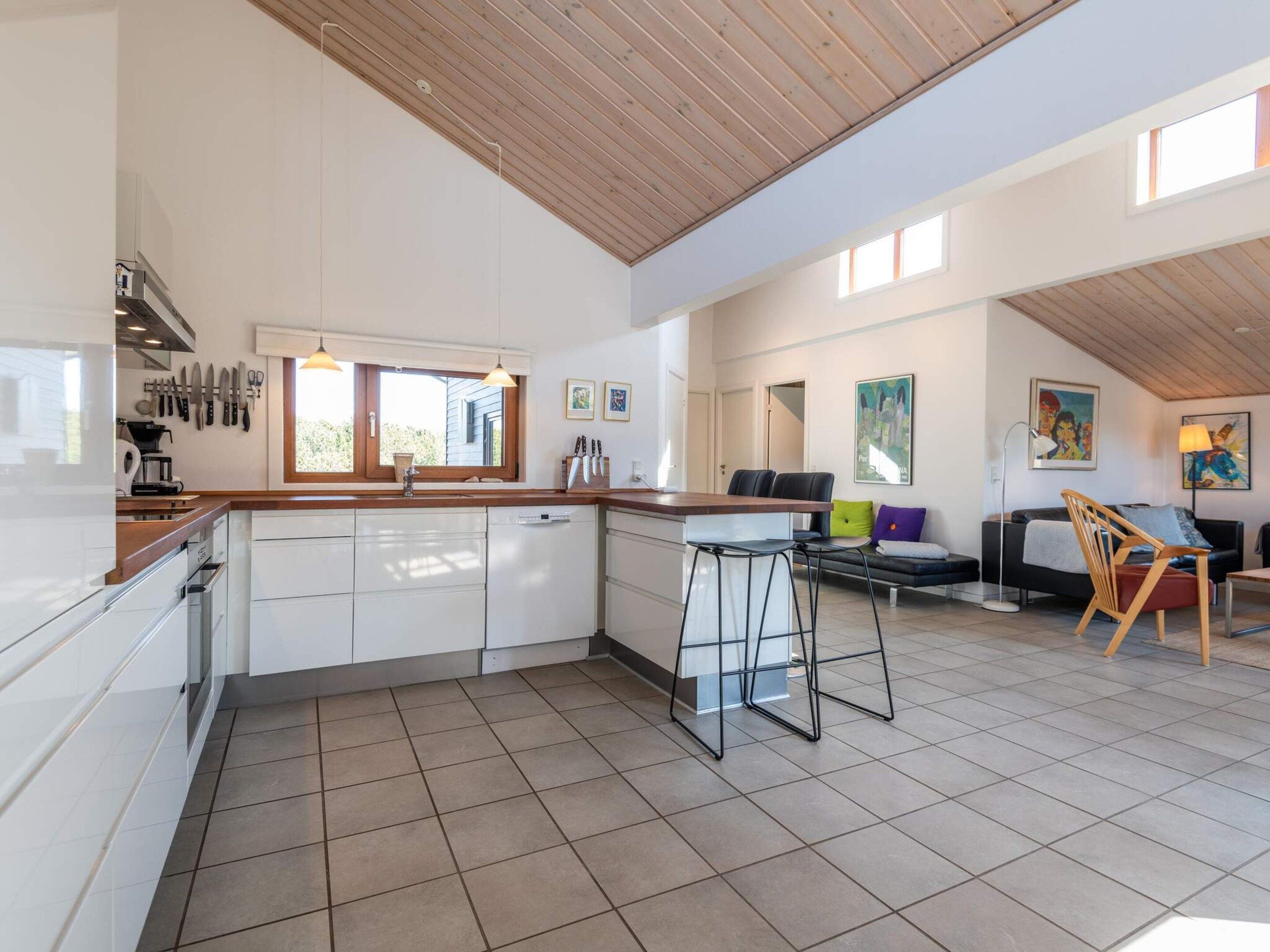 Une cuisine spacieuse avec un plafond en bois, un coin repas avec une table et des chaises hautes, et un salon avec un canapé et une lampe.