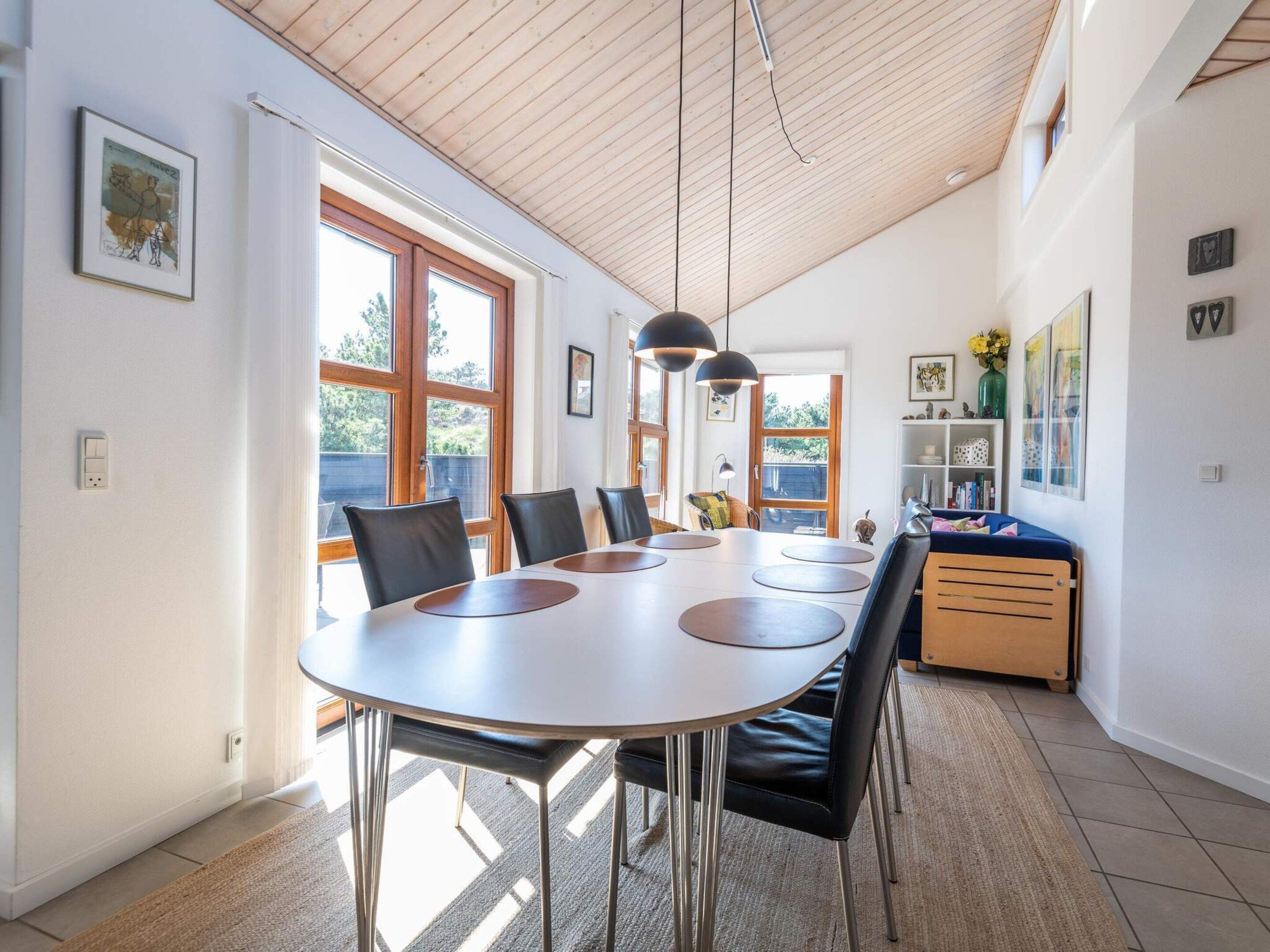 Un espace repas comprenant une table ronde, des chaises, des luminaires suspendus et une vue dégagée grâce à de grandes fenêtres.