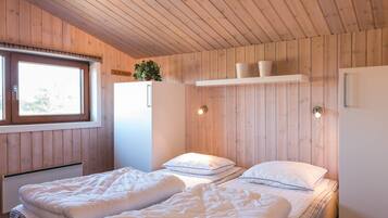 A bedroom with two beds, a window, a white wardrobe, and a shelf with decorative items.