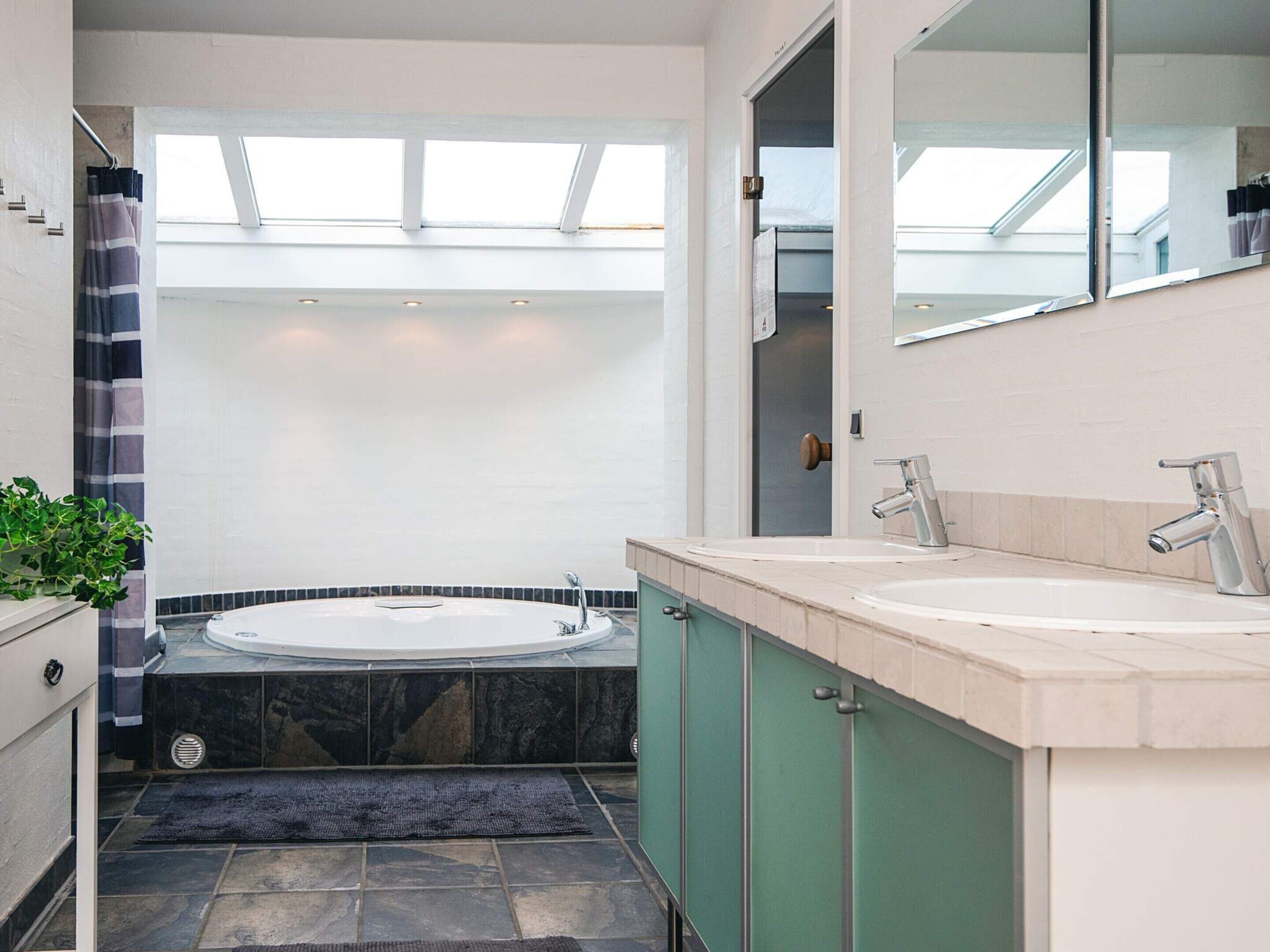 A modern bathroom with a freestanding bathtub, two sinks, a large mirror, and a skylight above.