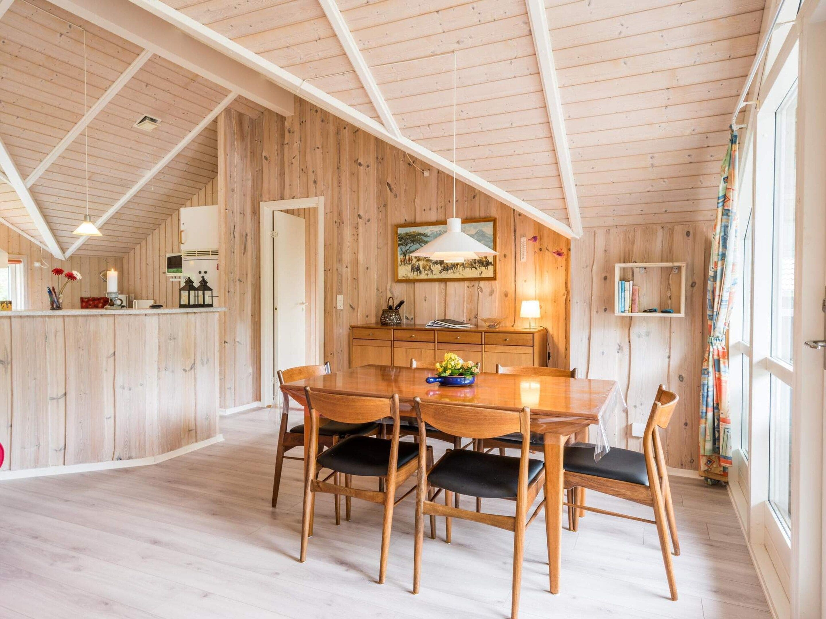 A wooden interior with a dining area, kitchen, and a large window.