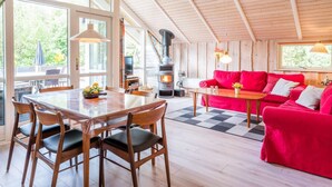 L’intérieur chaleureux d’un chalet avec un coin repas, un canapé rouge et un poêle à bois.