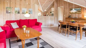Une pièce chaleureuse avec un canapé rouge, une table à manger en bois et un coin cuisine doté d’un bar.