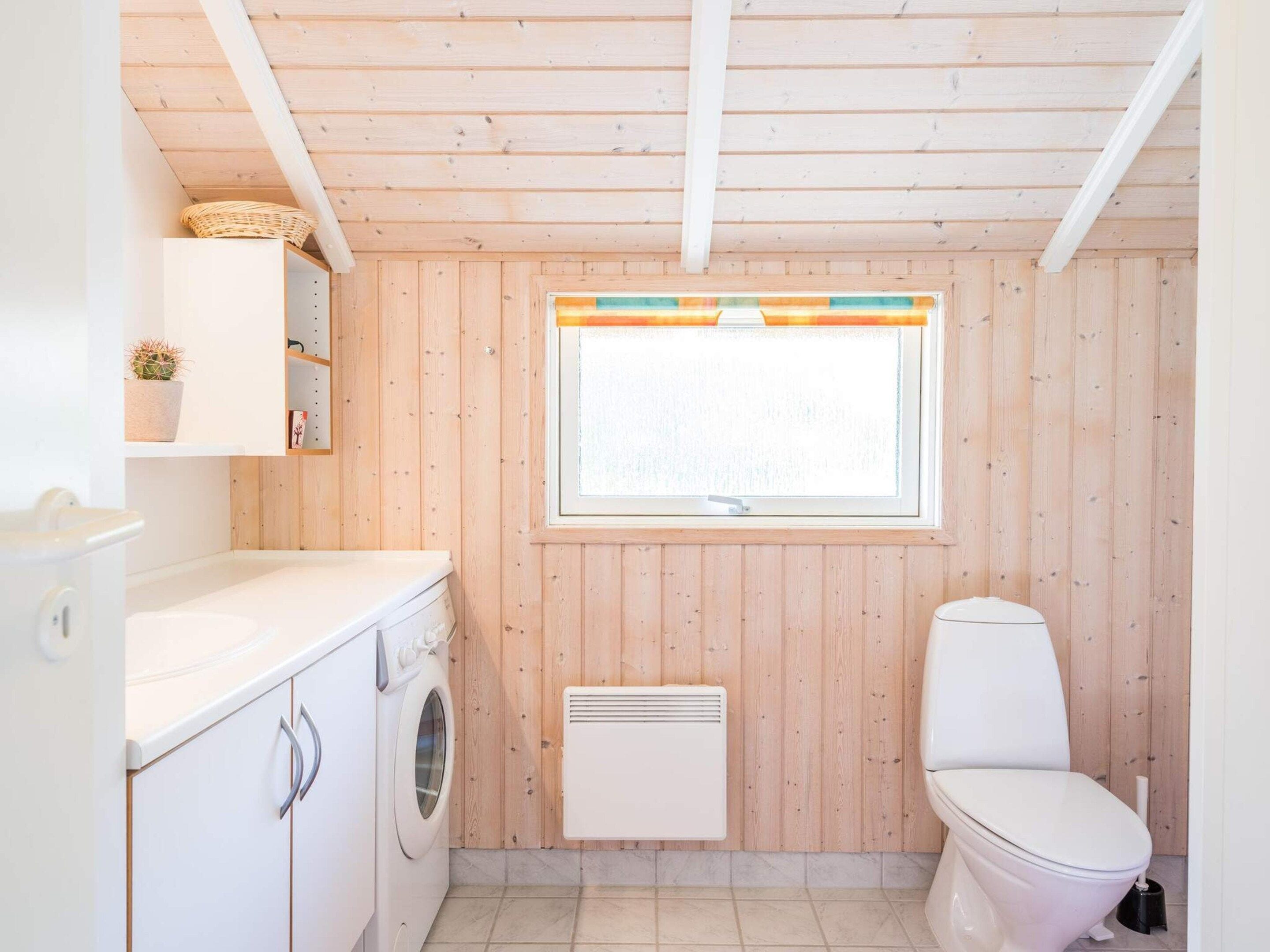 A compact bathroom with a washing machine, a toilet, and a window with a view.