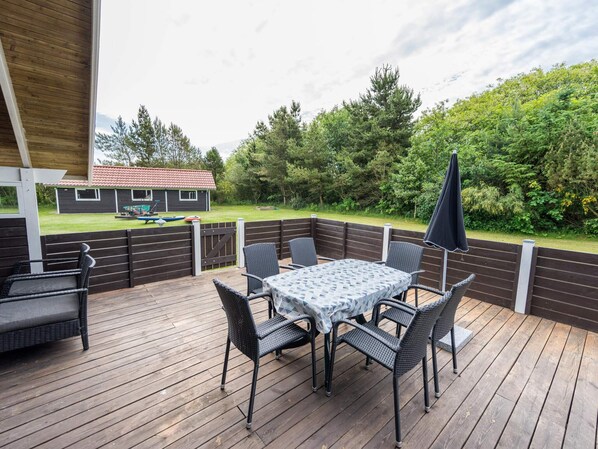 A wooden deck with a table and chairs, a covered area, and a view of a house and trees.