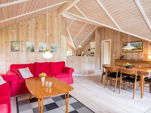 A cozy interior with a wooden ceiling, a red sofa, a wooden dining table, and a kitchen area.