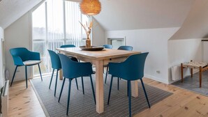 Un comedor con mesa de madera y sillas azules, una lámpara colgante y vistas amplias por las ventanas.