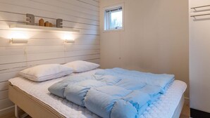Un dormitorio con una cama, cabecero con luces empotradas, un ventanal pequeño y suelo de madera.