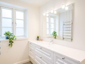 A modern bathroom with a white vanity, a large mirror, and two windows. - Holiday Home in Blåvand (Blavand)