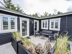 A modern outdoor patio with a black and white color scheme, featuring a seating area with a sofa and chairs, and large windows providing views of the surrounding area. - Holiday Home in Blåvand (Blavand)