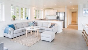 A spacious living area with a large striped sofa, a round coffee table, and a kitchen in the background. - Holiday Home in Blåvand (Blavand)