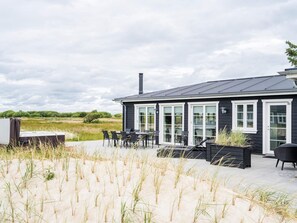 Un bâtiment noir doté de grandes fenêtres et d’une cheminée, entouré de dunes de sable et de végétation.