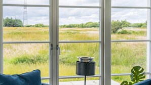 A room with a large window overlooking a grassy field and a transmission tower. - Holiday Home in Blåvand (Blavand)