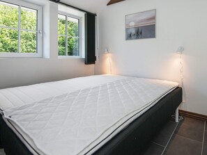 A bedroom with a bed, a window, a wall-mounted picture, and a bedside lamp.