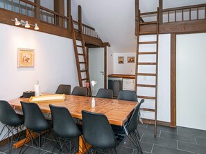 Un comedor con una mesa de madera, sillas negras y una escalera apoyada en la pared.