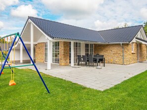 Ein Haus mit Terrasse, Steinmauern und einem Spielbereich.
