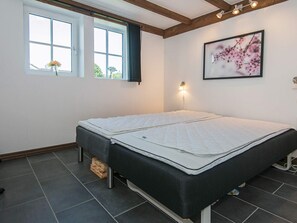 Ein Zimmer mit einem Bett, einem Vorhangfenster, einer Wandlampe und einem gerahmten Bild.