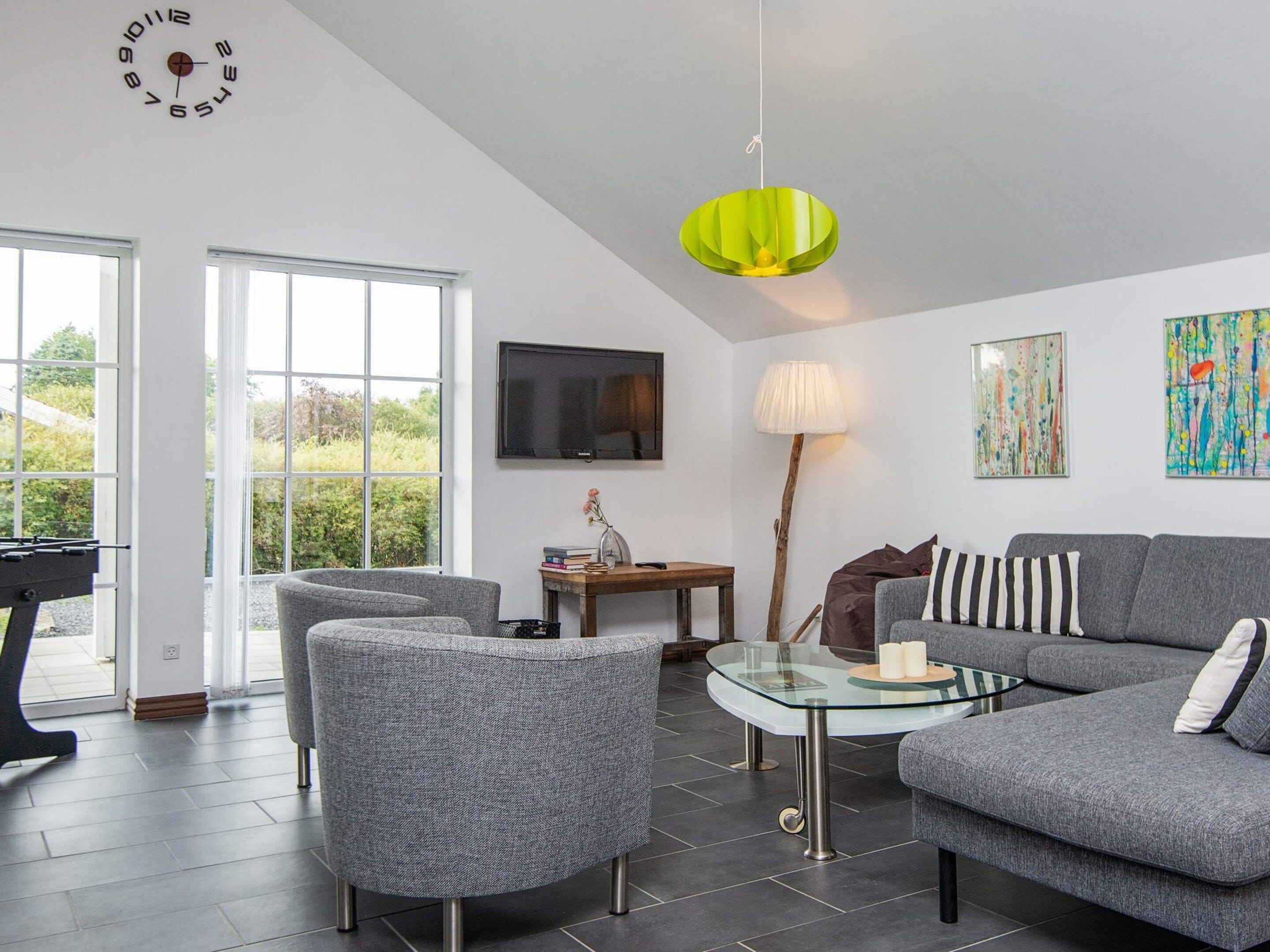 A modern living room with a sofa, armchairs, a glass coffee table, a television, and artwork on the walls.